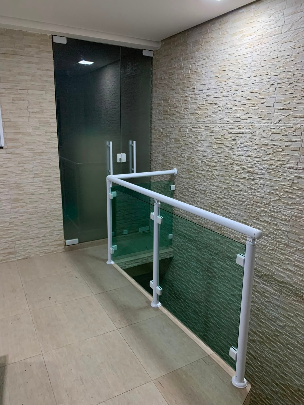 Guarda-corpo de vidro verde em corredor com parede de pedra